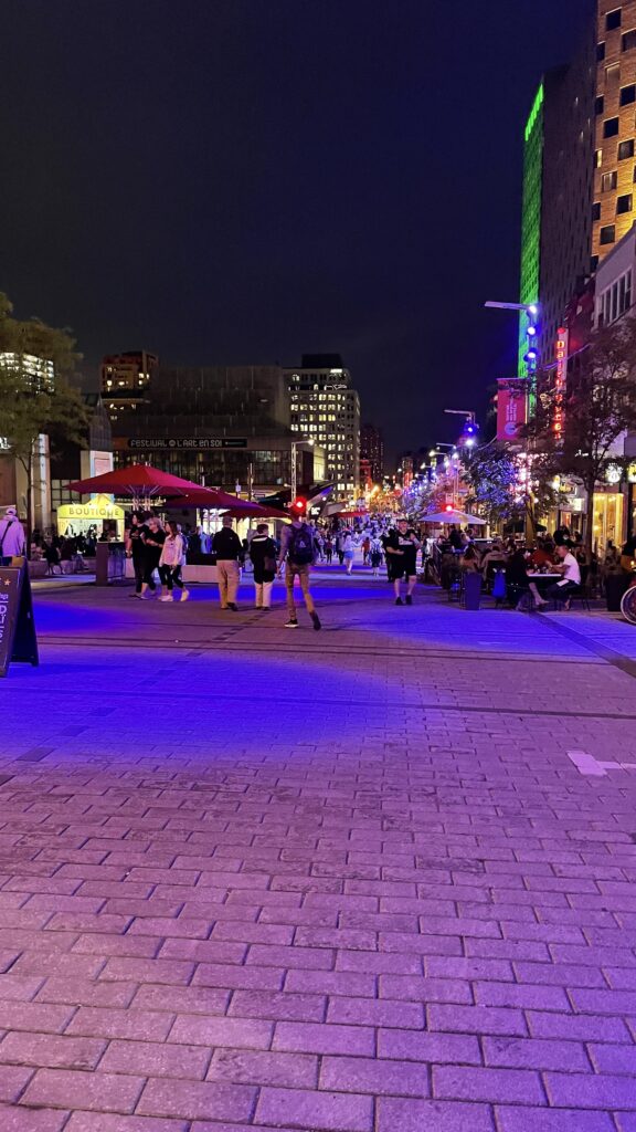 several lights, vendors and tourists walking amongst a popular Summer festival in downtown Montreal