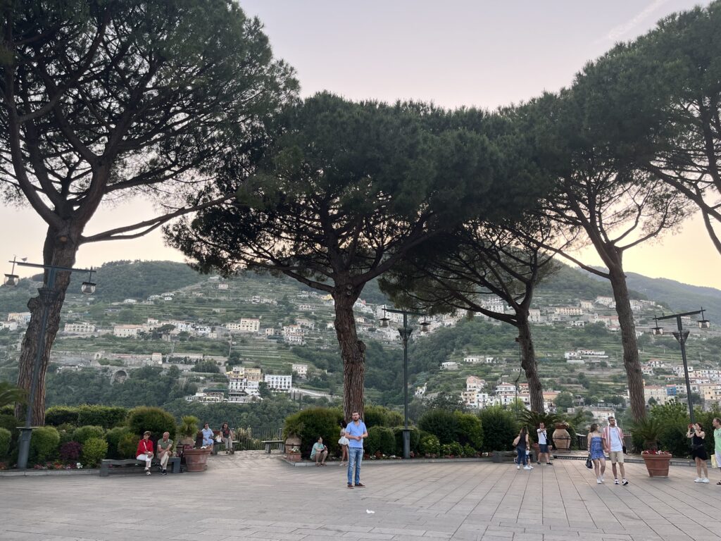 several locals and tourist sitting and walking in an open square area at sunset in Ravello, Italy
