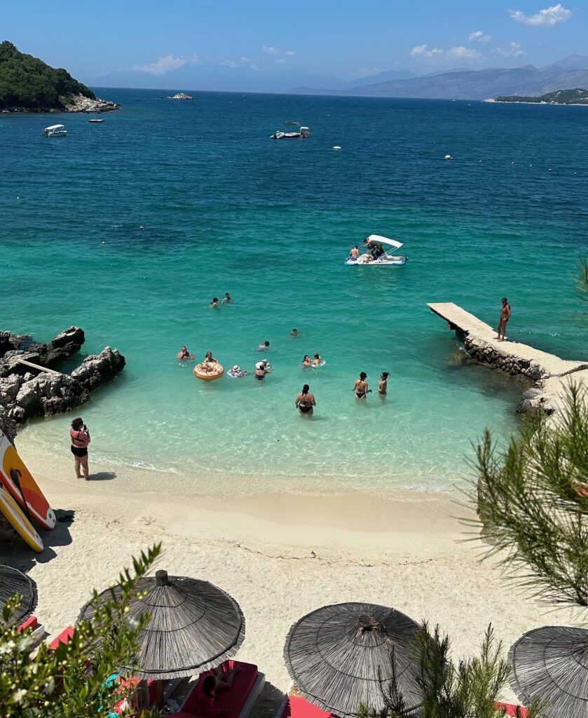 umbrellas, several tourists swimming in the crystal clear waters of Ksamil Beach in Albania, Is Ksamil worth visiting in Albania?  