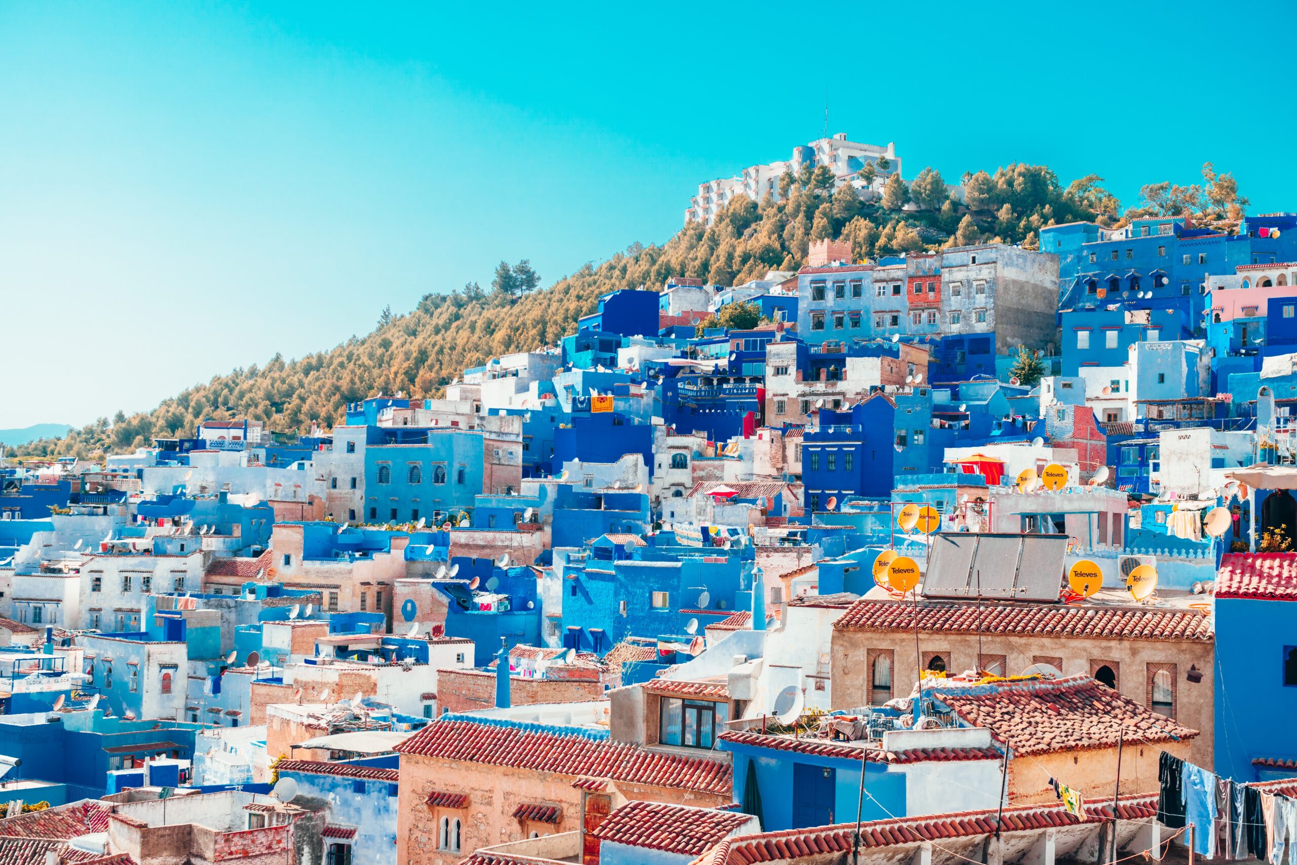 many blue homes sitting along the hills with mountainous range in the background in Chefchaouen, one of the cheapest cities in Morocco to visit