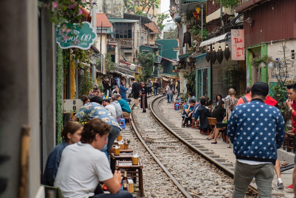 several tourist sitting on the side of a train track close by, the famous Hanoi train that passes within the city 