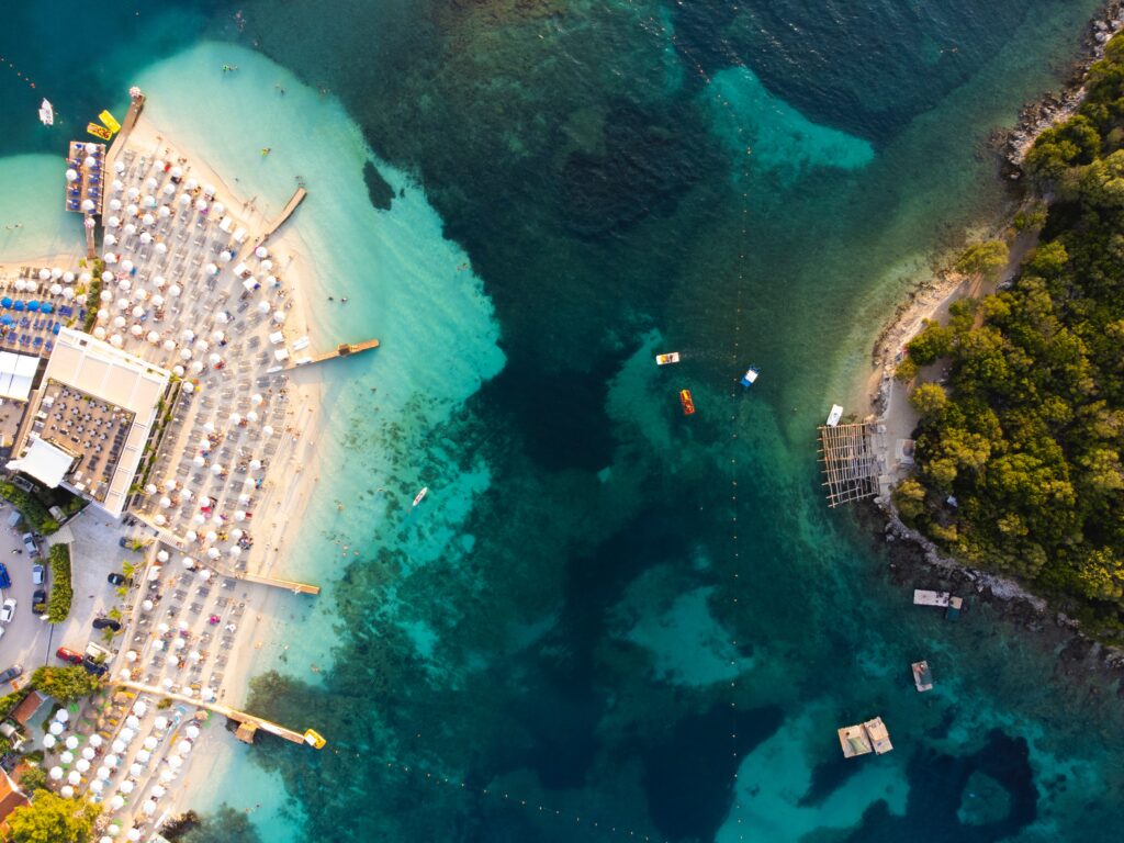 stunning aerial footage of the various shades of turquoise waters and a beach full of many tourist under their sun beds in Ksamil 