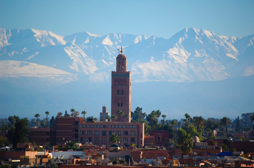 views of several buildings in the city centre of Marrakech, along with several mountainous ranges in the distance 