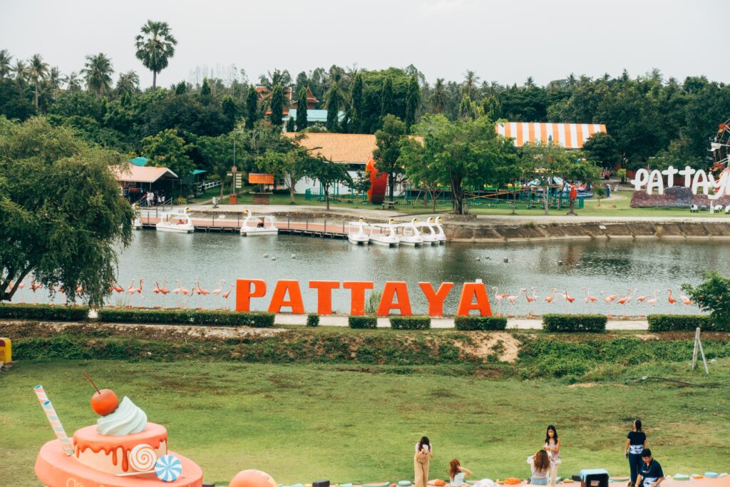 tourist walking around a greenery area at a park with the Pattaya sign by the river in the background 
