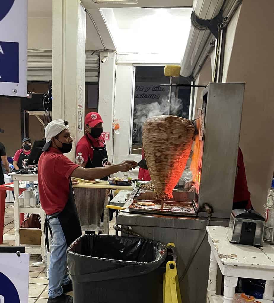 workers carving meat from a rotting meat spit for tacos in Playa Del Carmen