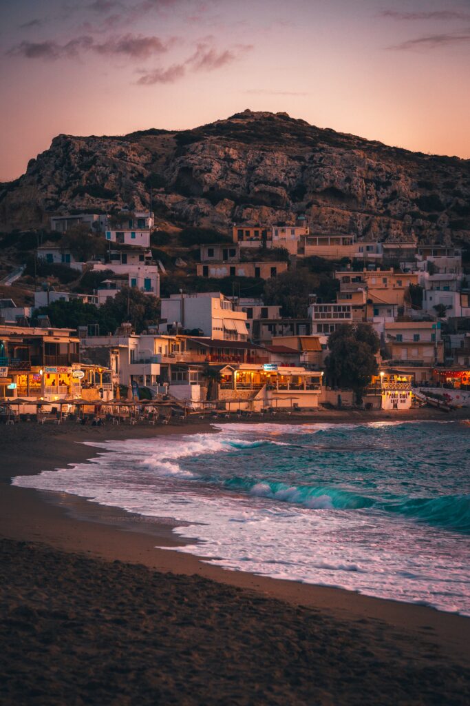 beautiful beach shoreline in Crete along with several restaurants and homes located amongst the hills