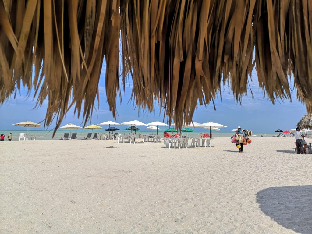many umbrellas on the beach and locals walking by in Progreso, Mexico by the shoreline 