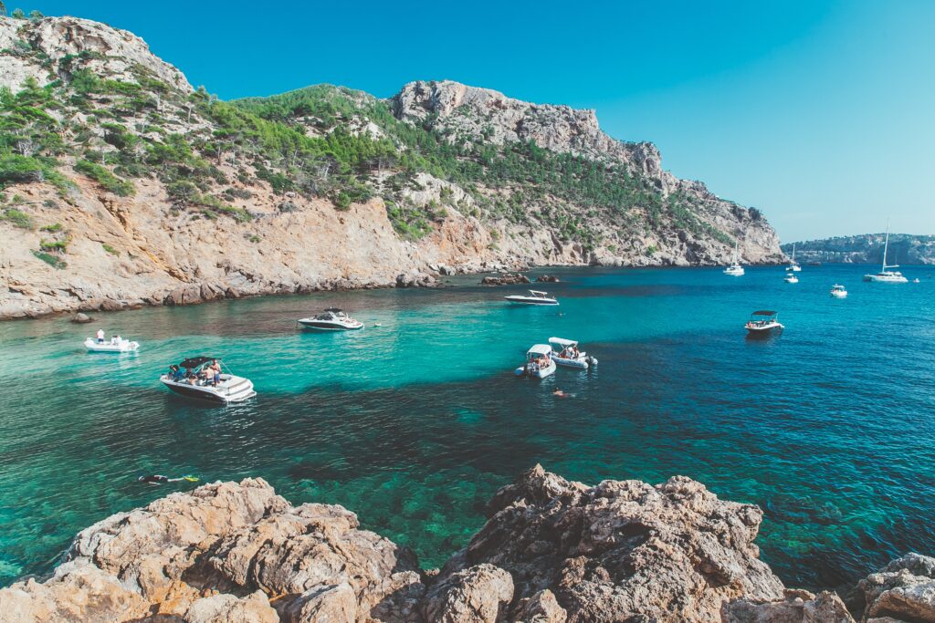 several hues of turqouise blue waters and several boats enjoying themselves on boats in Mallorca, Spain  