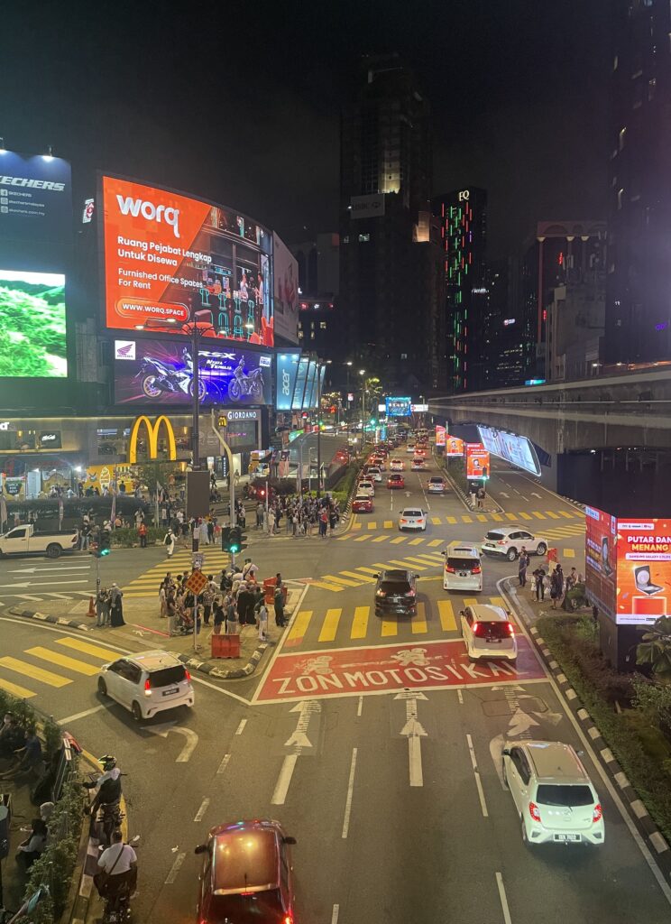 several tourists and locals crossing the street at night at a busy intersection in Kuala Lumpur 
