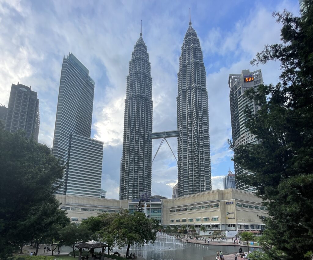 view of a pond area and the Petronas Towers on a clear sunny day in Kuala Lumpur, Malaysia / Is Kuala Lumpur expensive to visit