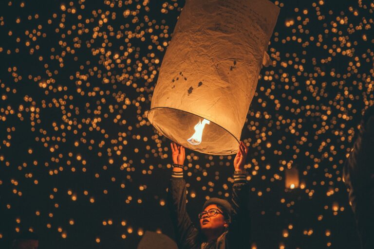 person releasing a illuminated lantern into the dark sky full of several other lanterns during Yi Peng festival / one of many festivals in Chiang Mai