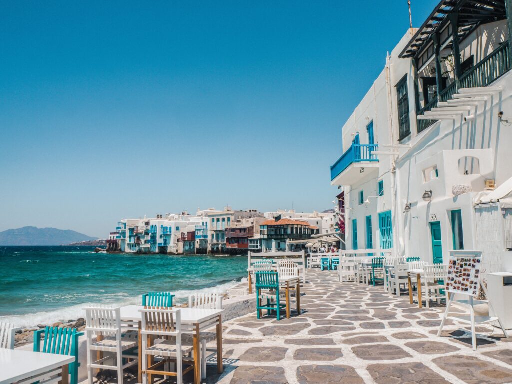 a charming picturesque street with dining tables nearby a stunning coastline in Mykonos, Greece