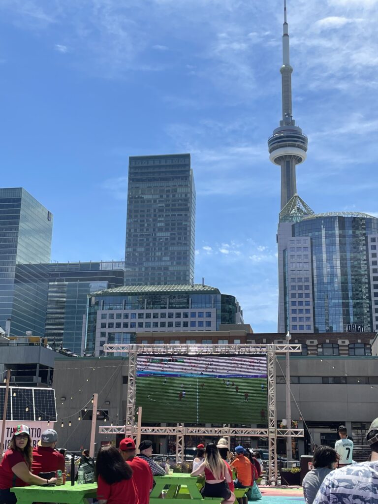 outdoor restaurant showing a soccer game along with the Toronto city skyline in the background 