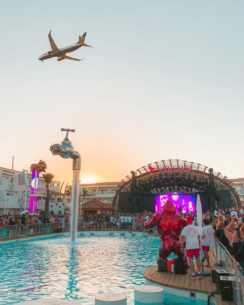 large crowd at a sunset party in Ibiza with a plane flying above on it's way to land in Ibiza, Spain 