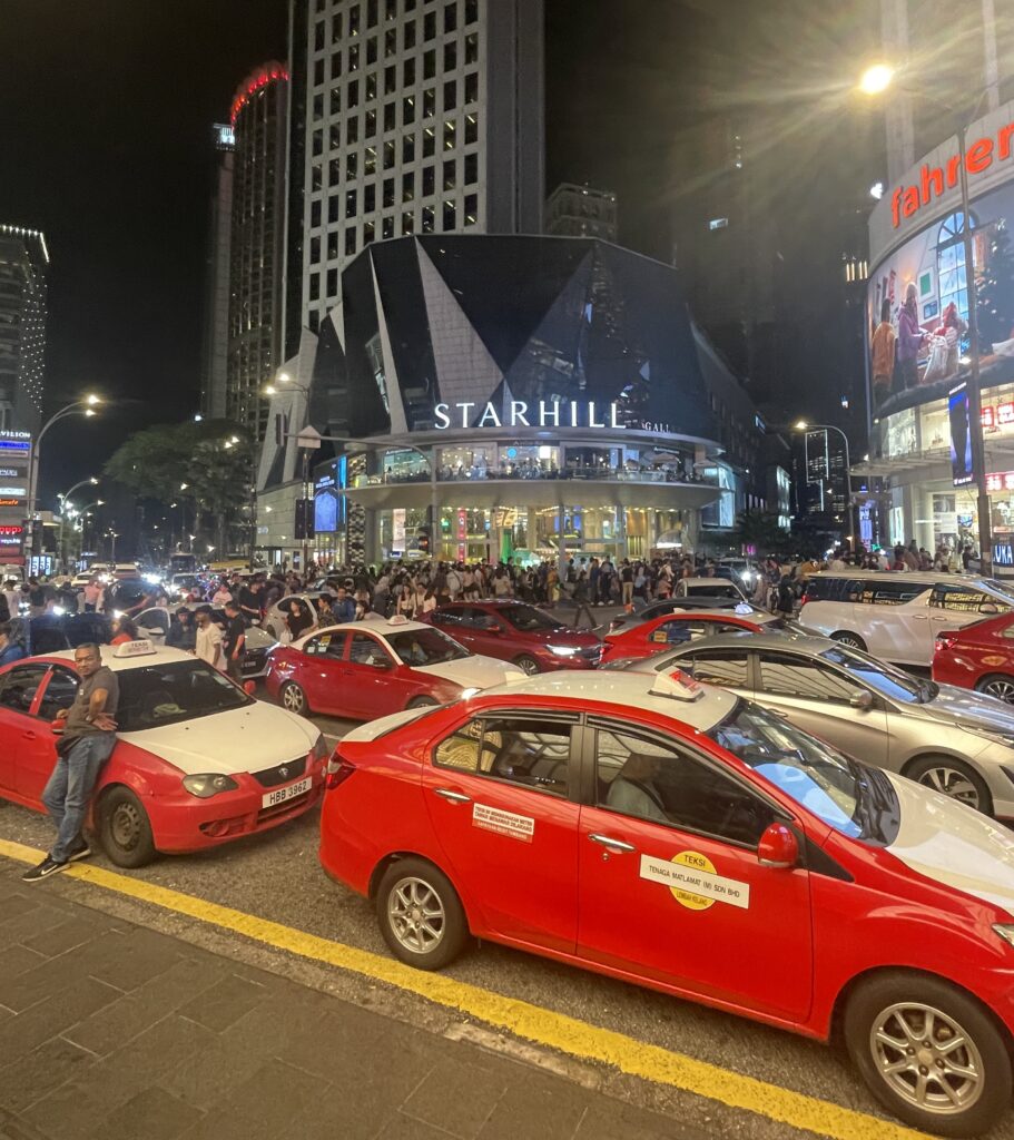 classic red and white Malaysian taxis parked outside of a popular mall waiting for customers
