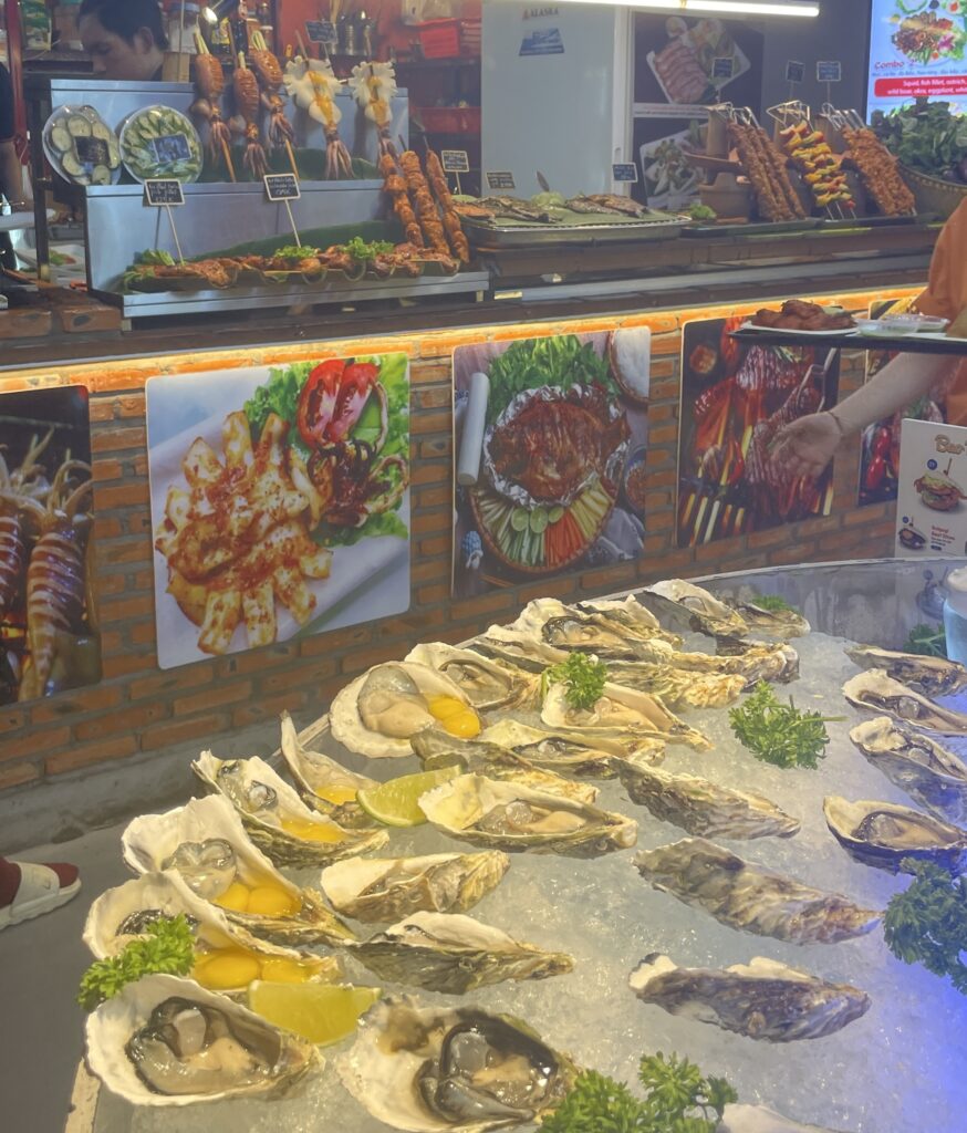 oysters sitting on ice at a stall at the food market in Ho Chi Minh with many options of various meats being sold in the distance at another food stall at the food market 