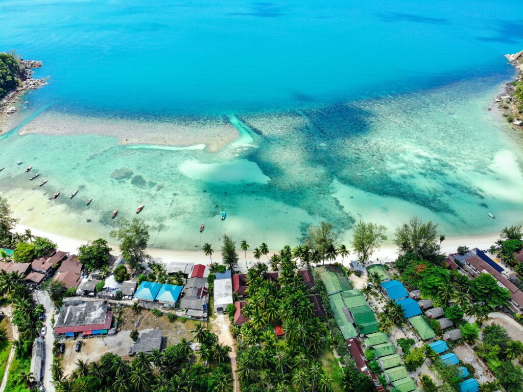 aerial shot of a beach in Koh Phangan, Thailand with several hues of turquoise waters / how to get around Koh Phangan