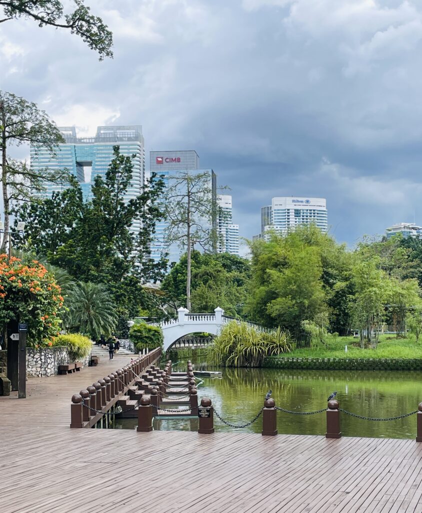 a charming white bridge over a small lake shown in the distance amongst plenty of greenery at the Perdana Botanical Gardens in Kuala Lumpur