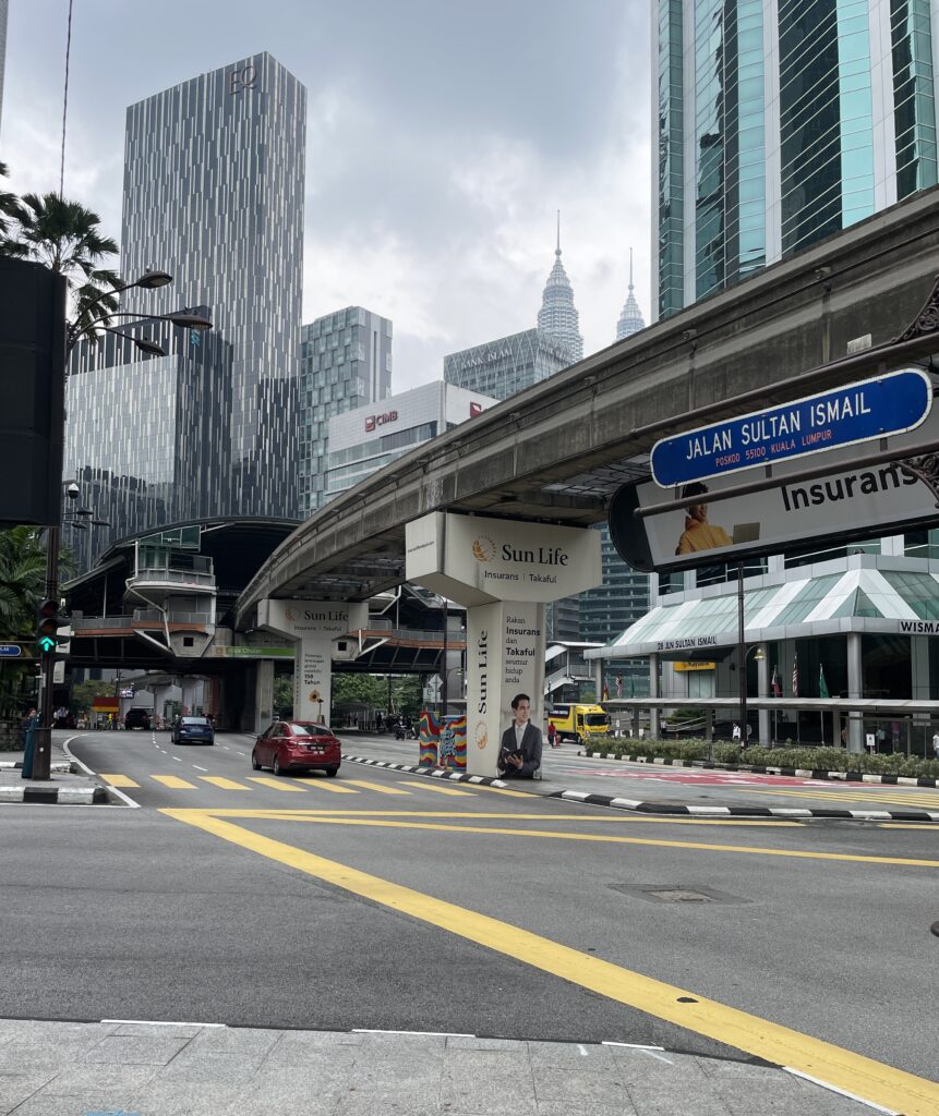 street intersection in Kuala Lumpur with many tal lbuildings in the distance and a sky train track for the city's public transportation 