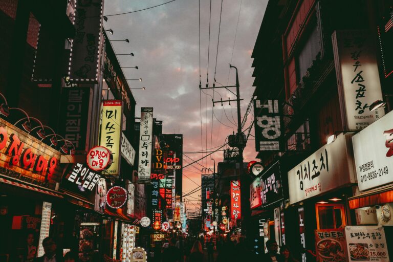 many neon lights of store signs on a street during the evening in Seoul, South Korea