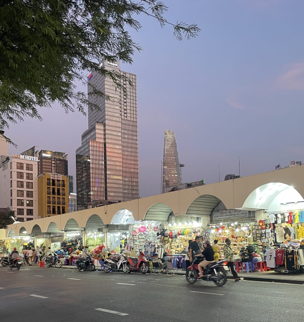 the vibrant Ben Thanh Market from the outside amongst many skyscraper buildings during a vibrant sunset in Ho Chi Minh City