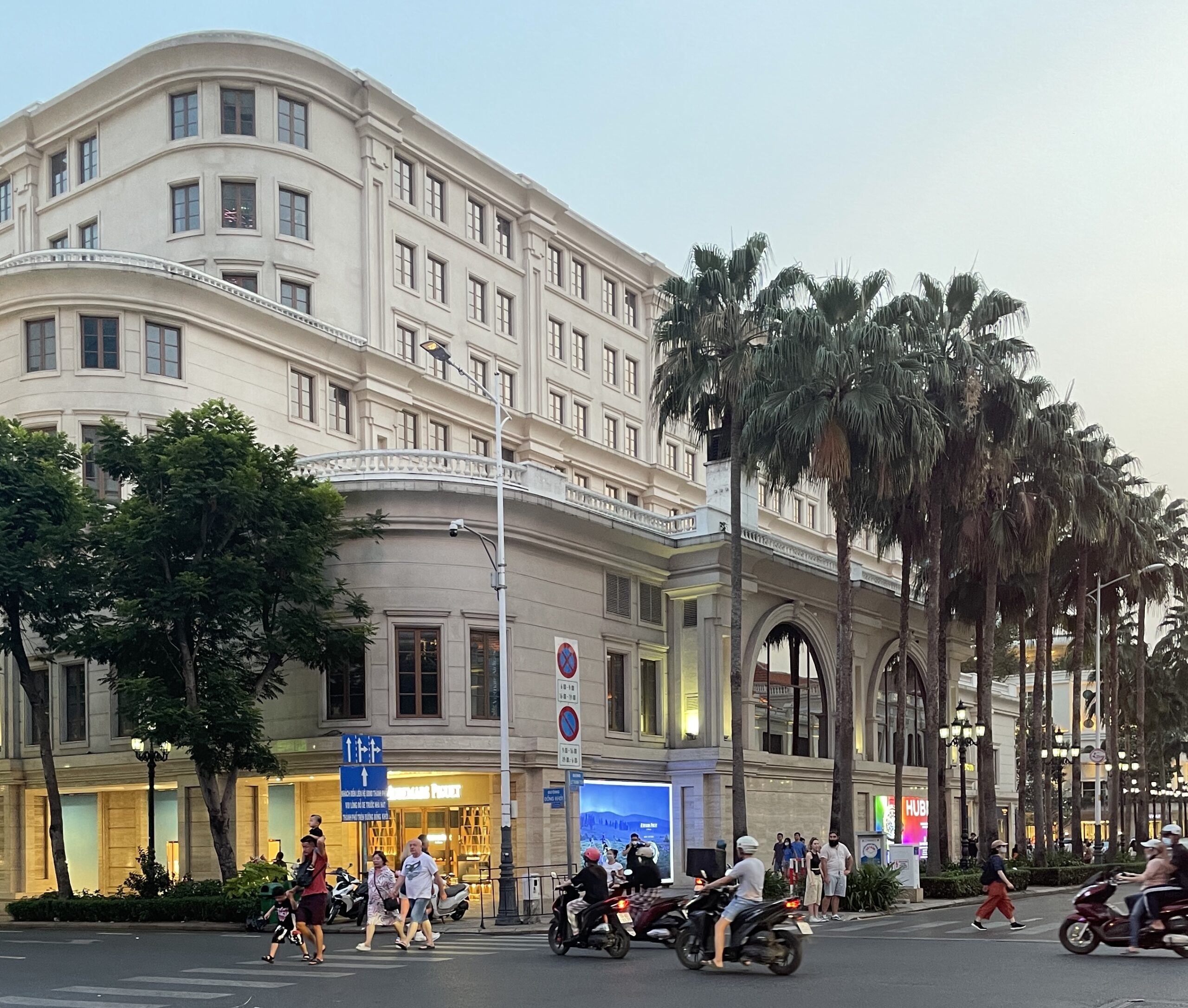 scooters driving by as tourists cross the streets in Ho Chi Minh City in the evening / best and worst time to visit Ho Chi Minh City