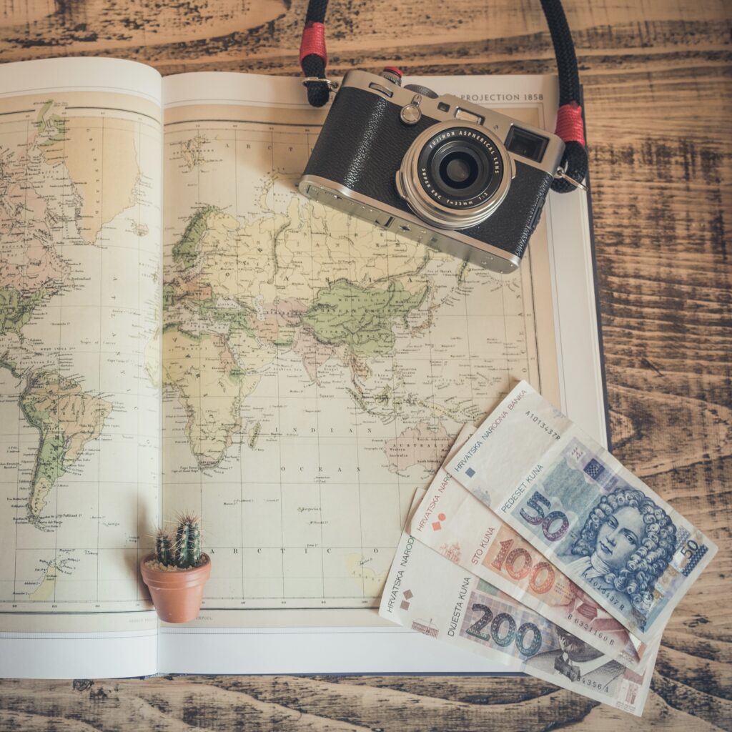 a book with a large world map, an old camera and currency bills, the beginning stages of travel planning