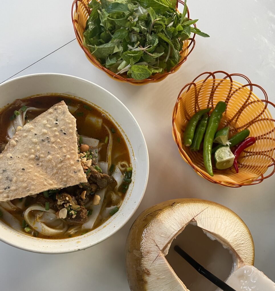 mi quang dish being served alongside a fresh coconut