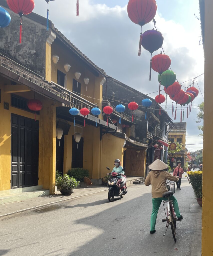 a woman biking in the streets amongst yellow painted buildings in Hoi An, Vietnam