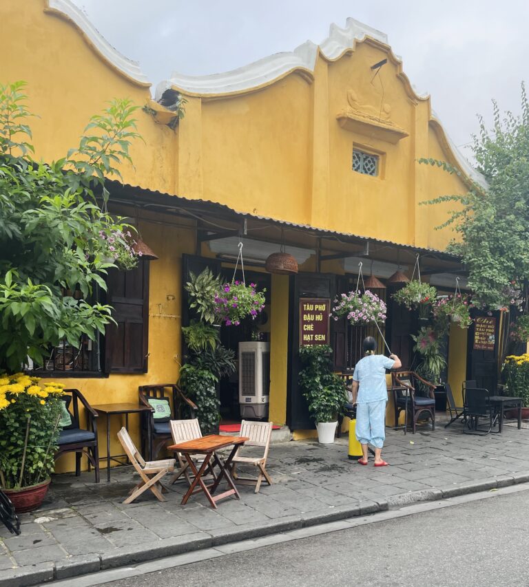 a local woman sweeping the floor at a ancient yellow painted home in Hoi An