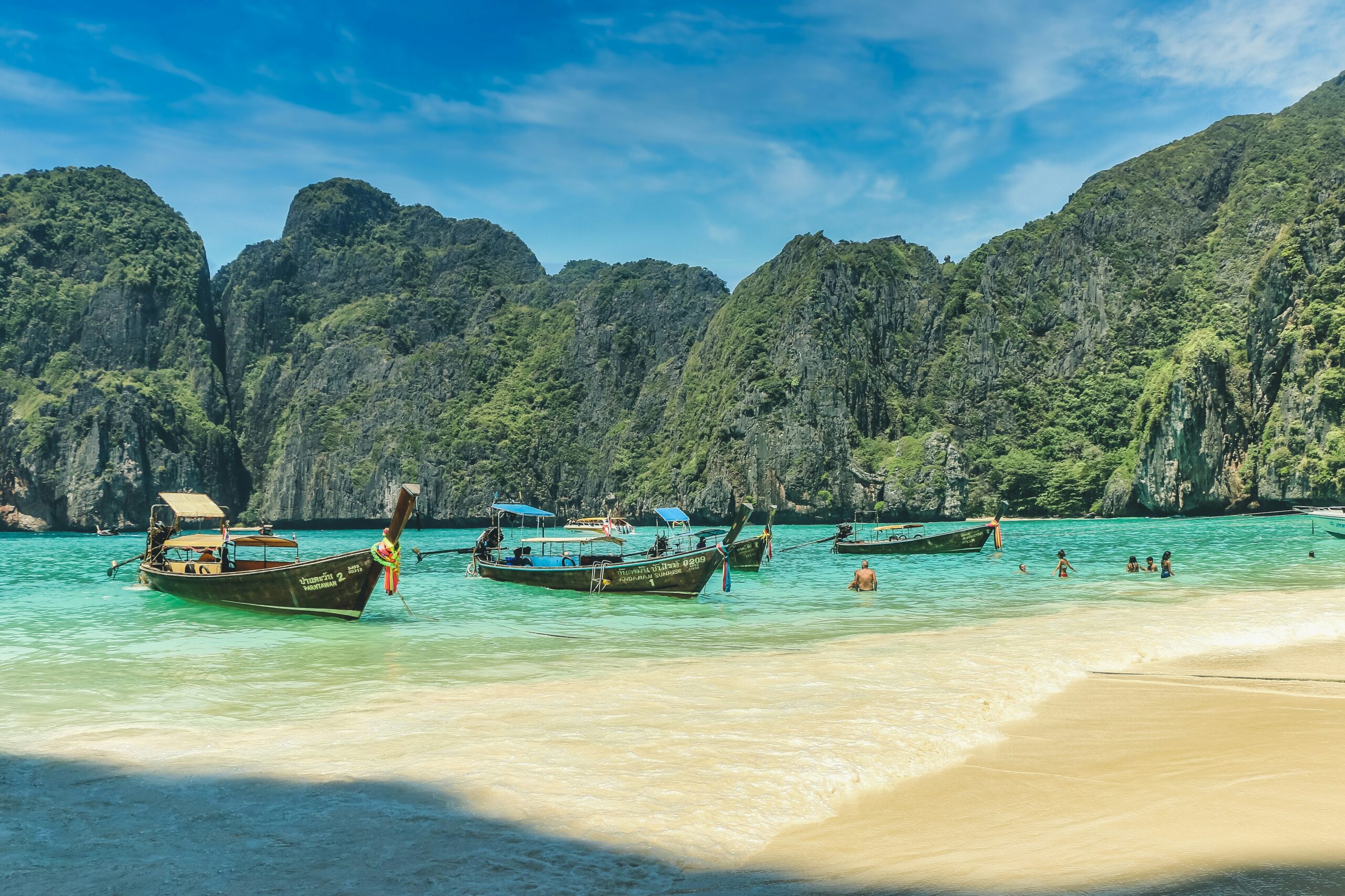 Traditional longtail boats floating in crystal-clear turquoise water with limestone cliffs in Krabi, Thailand