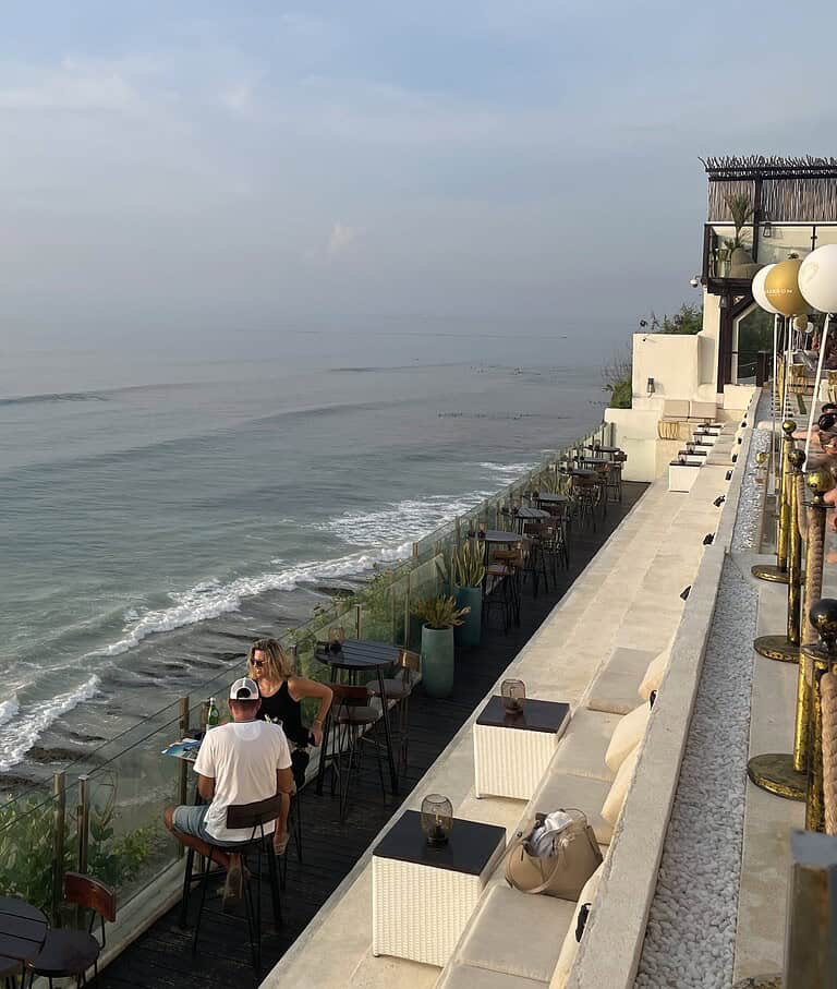Sunset view from a cliffside beach club in Bali overlooking the ocean, with golden skies and waves crashing below, captured during the best time to visit Bali.