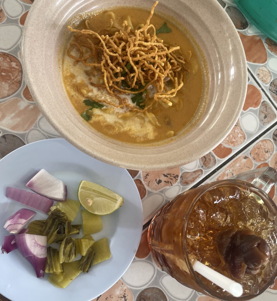 A flavorful bowl of beef Khao Soi with thin noodles, served alongside a refreshing glass of longan Thai juice in Chiang Mai.