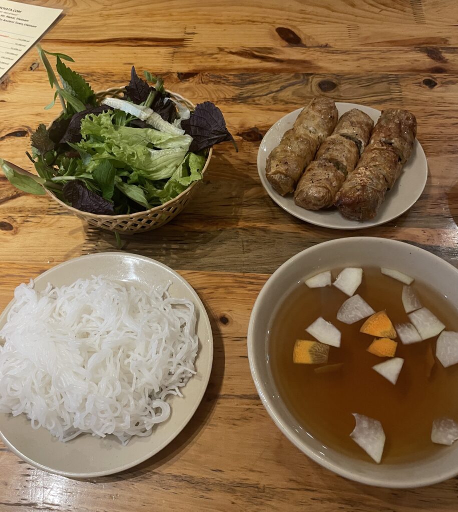 A variety of Bun Cha-style dishes served on a table in Hanoi, featuring grilled pork, noodles, and fresh herbs.