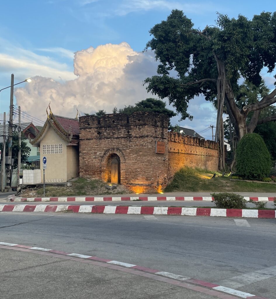 Beautiful ancient Old City walls in Chiang Mai during sunset, with glowing clouds and a silhouetted tree in the foreground.