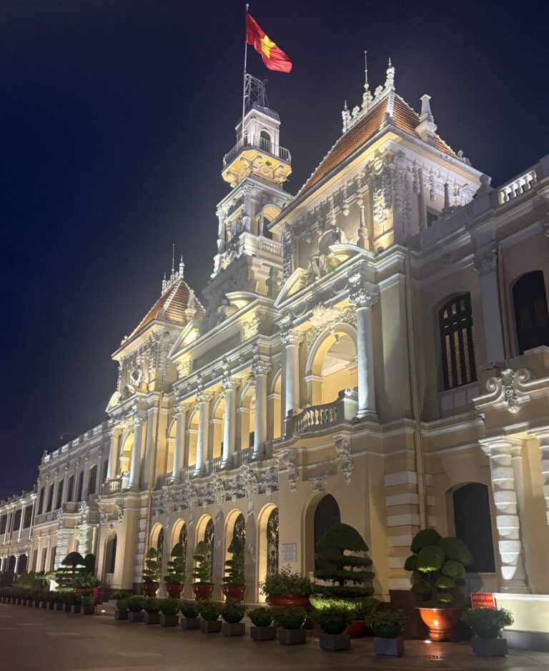 Ho Chi Minh City People’s Committee building beautifully illuminated in the evening, framed by manicured gardens and trees.