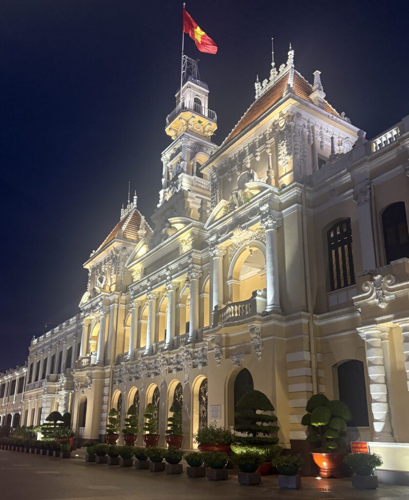 Ho Chi Minh City People’s Committee building beautifully illuminated in the evening, framed by manicured gardens and trees.
