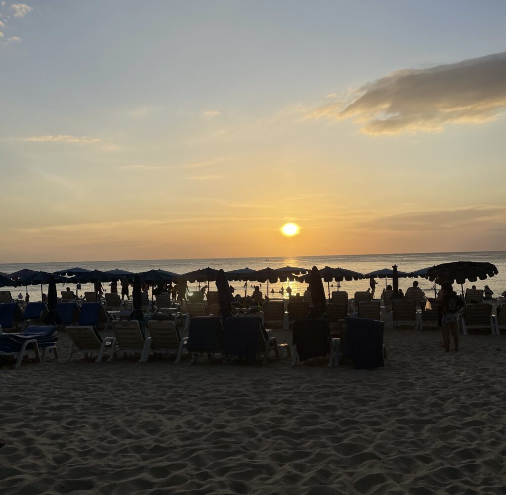 a stunning sunset with several locals and tourist viewing it on Karon Beach, Phuket, Thailand