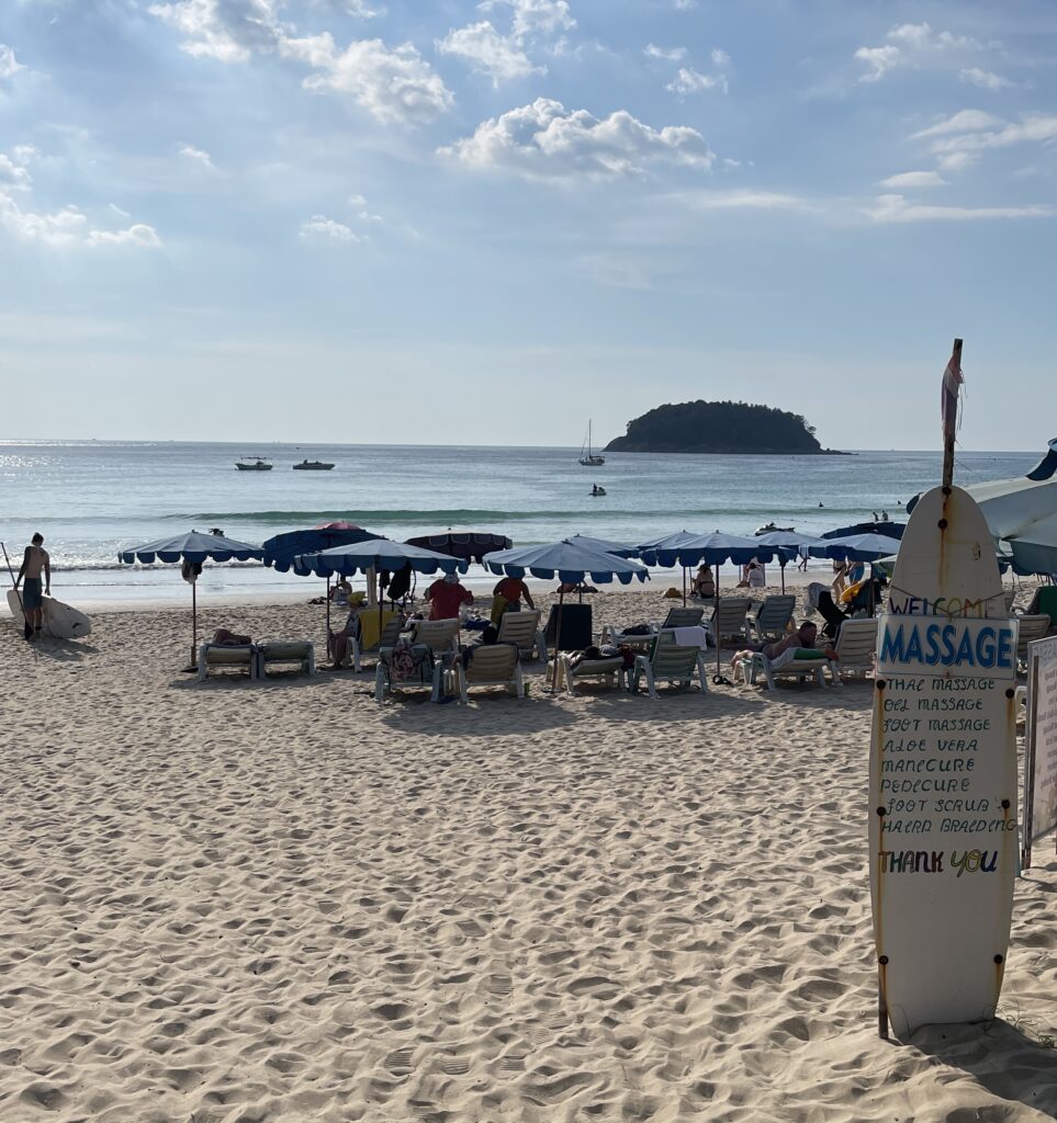 Surfboard with massage ad on Kata Beach surrounded by beach chairs in Phuket, Thailand