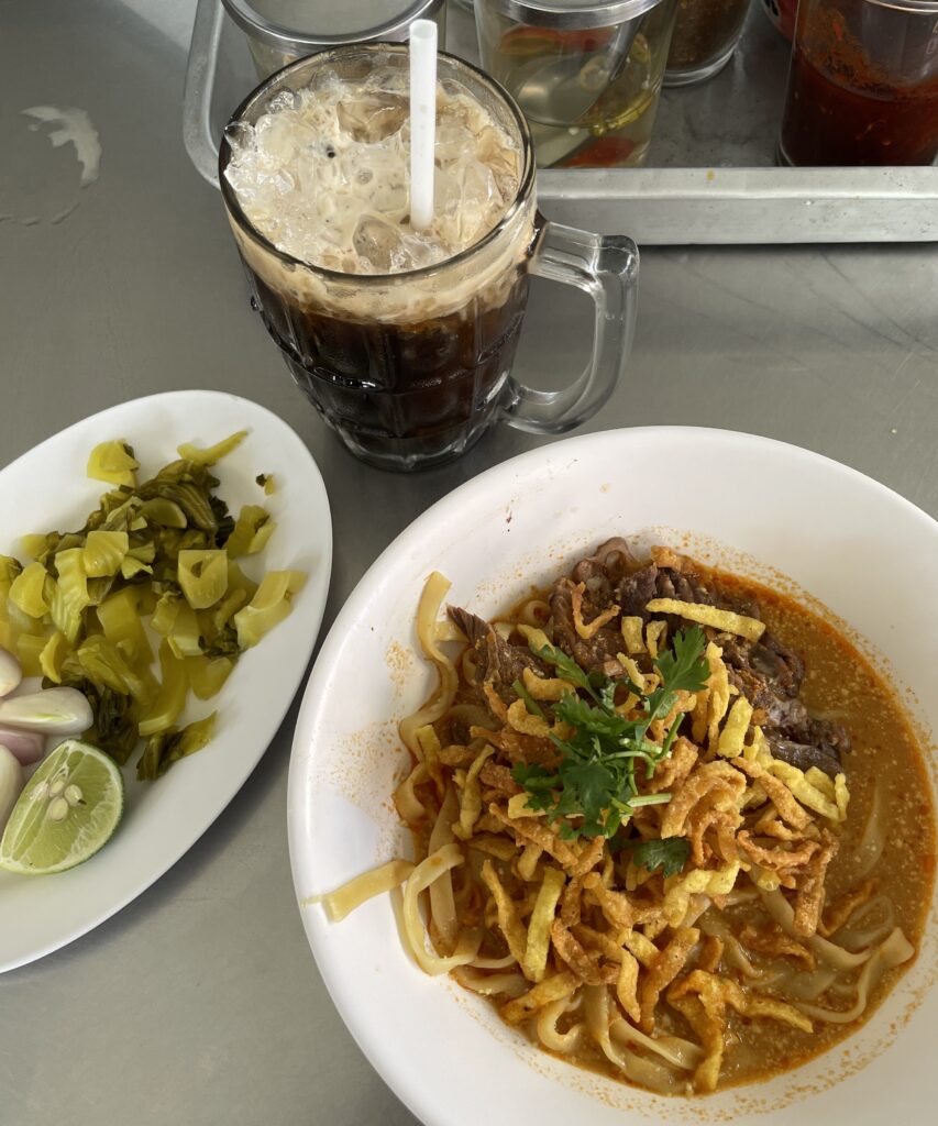 Khao Soi served at Khao Soi Maesai in Chiang Mai, paired with a classic Thai iced coffee for the perfect local meal experience.
