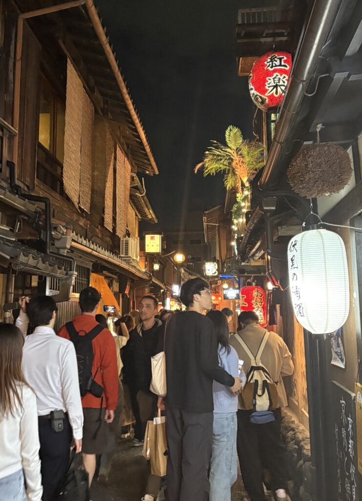 Busy Kyoto street at night filled with tourists, illuminated by storefront lights and traditional signage.