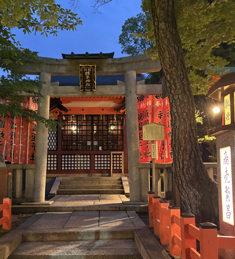 Traditional Japanese temple arch at dusk in Kyoto, with a stone pathway leading through soft evening light and ambient lantern glow