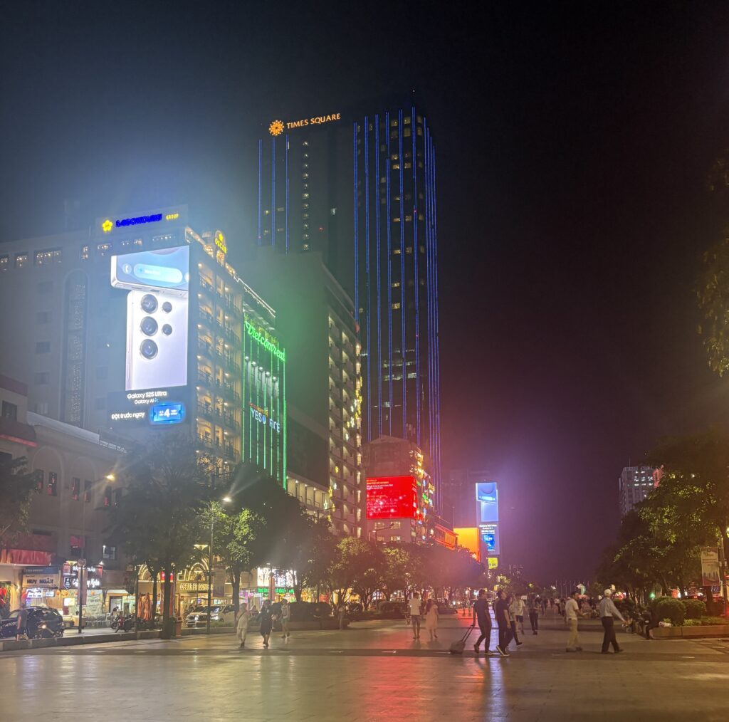 Locals and tourists walking along Nguyen Hue Walking Street at night with bright lights, ads, and a lively atmosphere in Ho Chi Minh City