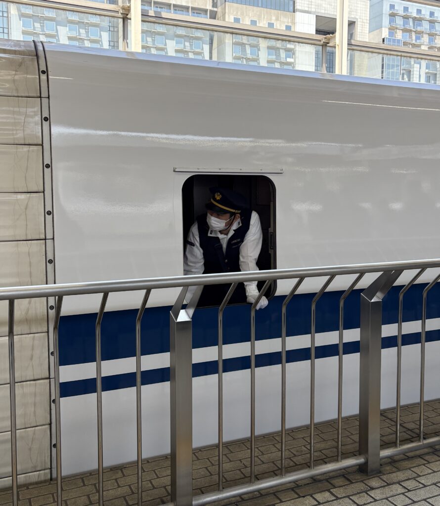 View from a bullet train window in Osaka with a uniformed train worker visible in the foreground