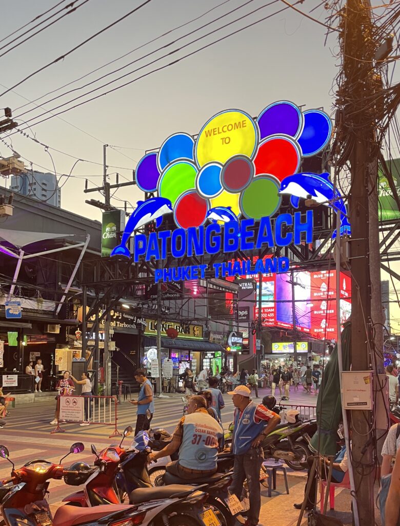 Patong Beach sign glowing at golden hour with evening lights in Phuket, Thailand