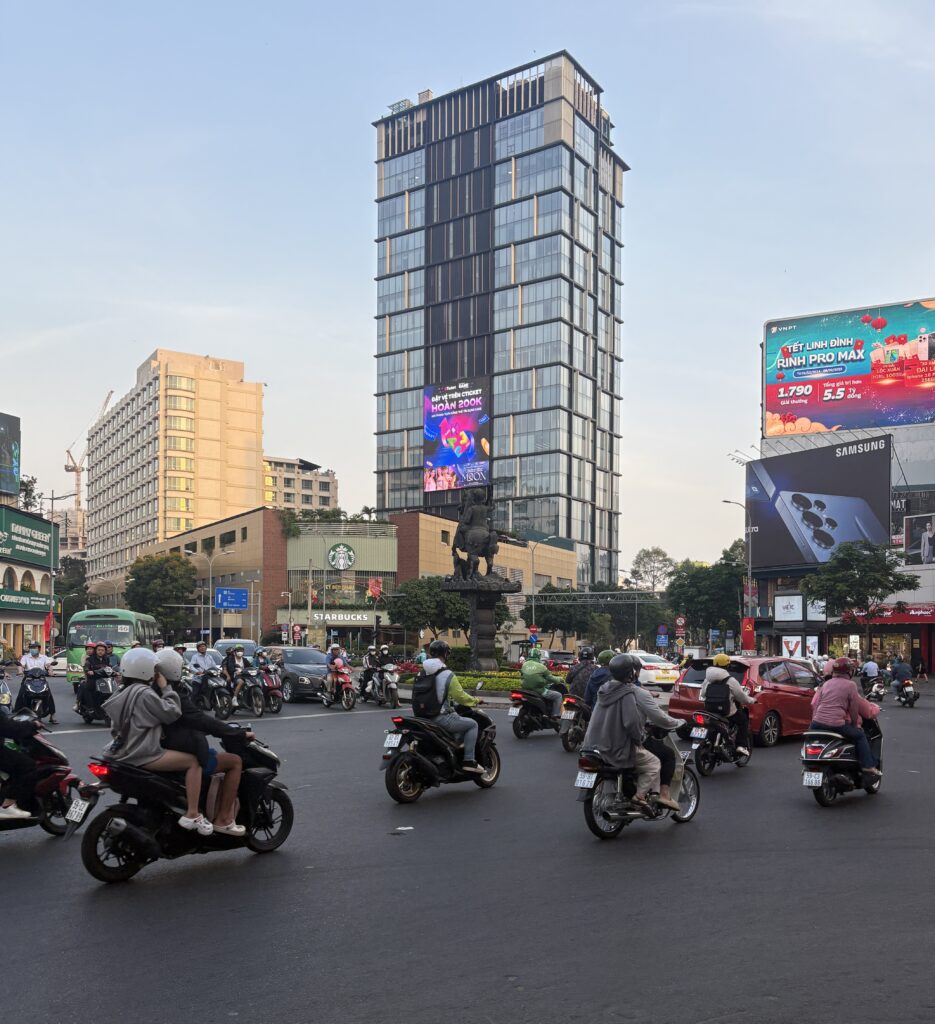 Many locals riding scooters through a busy roundabout in Ho Chi Minh City, showcasing typical traffic scene