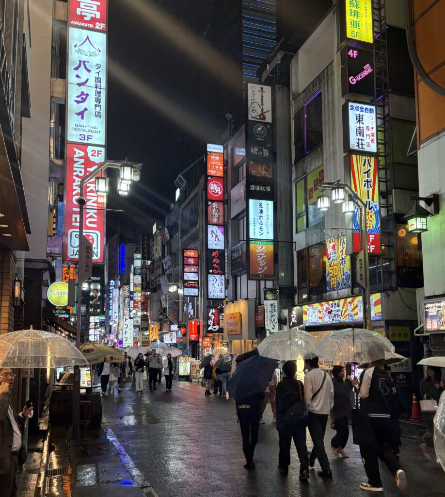 Rainy night in Shinjuku, Tokyo with crowds walking under clear umbrellas surrounded by glowing neon signs