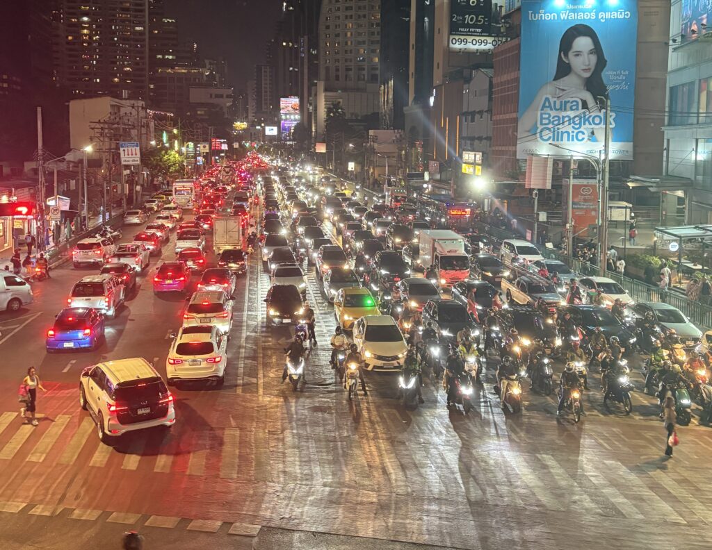 Nighttime view of heavy Bangkok traffic with cars and scooters seen from an elevated skywalk near the BTS Skytrain