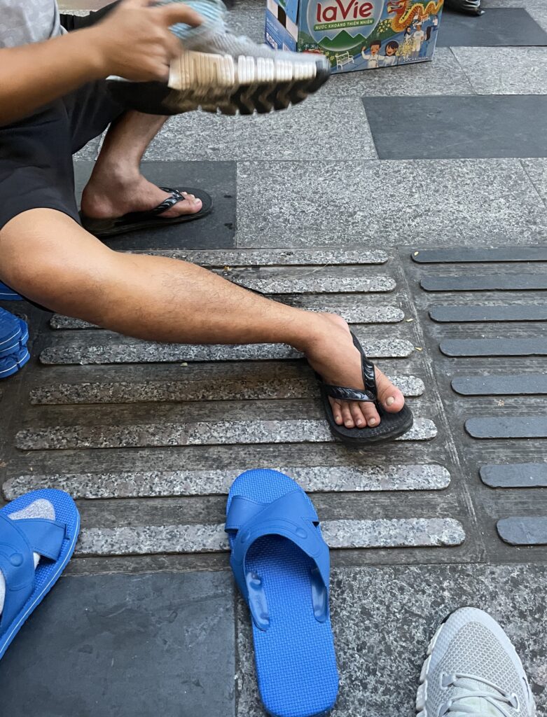 Street shoe shiner cleaning a tourist’s shoes in Ho Chi Minh City, Vietnam.