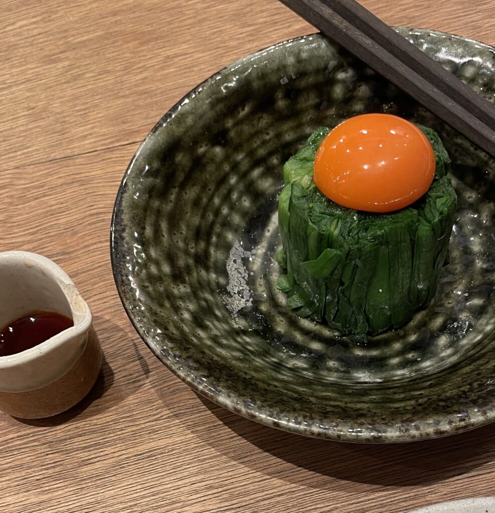 Unique Japanese izakaya dish of spinach topped with raw egg yolk, beautifully plated.